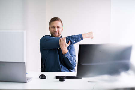 Close-up Of A Young Businessman Stretching His Arms At Workplace