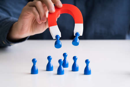 Businessman's Hand Attracting Blue Human Figures Standing In A Row With Horseshoe Magnetの写真素材