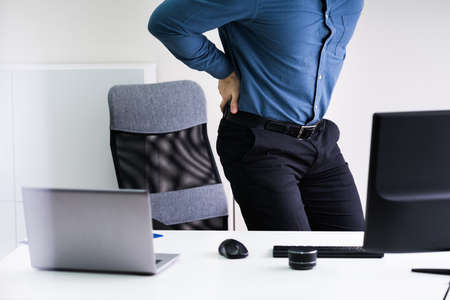 Businessman With Lower Back Ache Standing Near Office Deskの写真素材