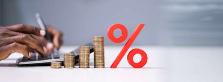 Close-up Of Red Percentage Symbol In Front Of Businessperson Calculating Invoice