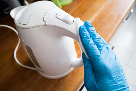 Man Wiping Electric Tea Kettle Handle With Sanitizer Against Virus Infection