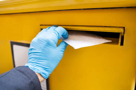 Man Inserting Letter In Mailbox Wearing Gloves To Protect From Coronavirus