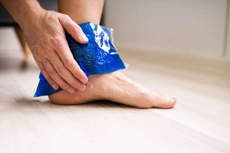 Close-up Of Person's Hand Holding Ice Gel Pack On Ankle At Homeの写真素材