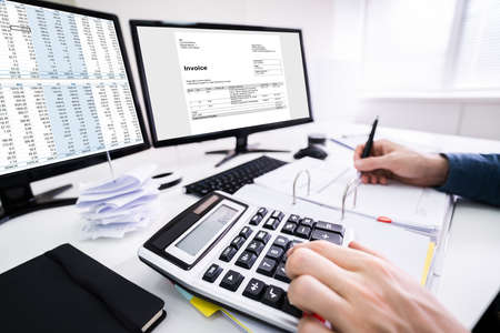 Young Businessman Calculating Bill With Computer And Laptop On Deskの写真素材