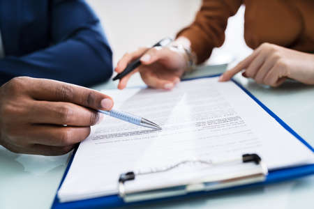 Two Businesspeople Hand Analyzing Document Over Glass Desk