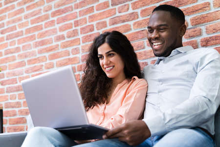 Portrait Of A Happy Young Couple Sitting On Couch Using Laptopの写真素材