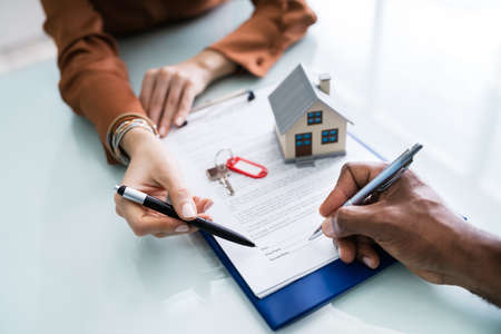 Close-up Of A Person's Hand Signing Contract With Keys On Itの写真素材