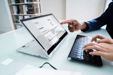 Businessman Pointing Invoice On Laptop Screen To Her Male Colleague While Working In Office
