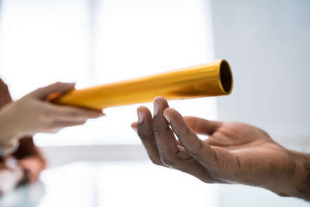 Close-up Of Businessman's Hand Passing The Golden Baton To His Partner In Officeの写真素材