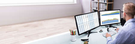 Analyst Looking At Data Table Report On Computer Desk