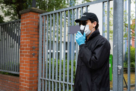Security Guard In Face Mask Talking On Walkie Talkie