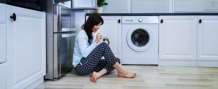 Hungry Pregnant Woman Eating Food At Night Near Refrigeratorの写真素材