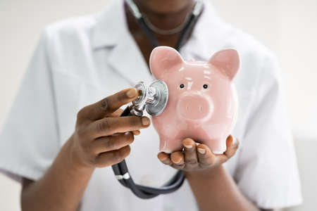 African Doctor Examining Savings In Piggybank Using Stethoscopeの写真素材