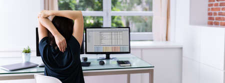 Woman Stretches At Office Desk Chair While Working