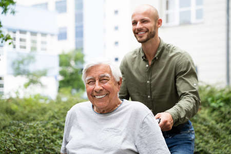 Old Smiling Senior Wheelchair Transport In Park