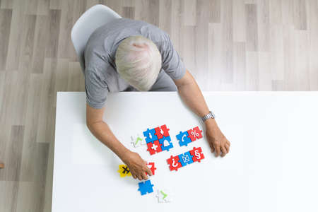 Elder Man Playing Jigsaw Puzzle On Tableの写真素材