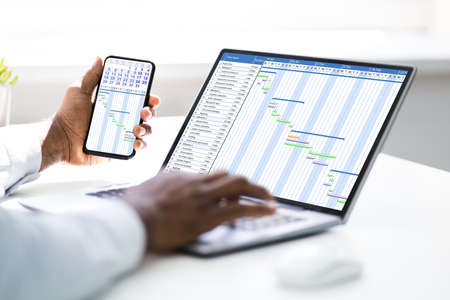 African American Using Online Time Sheets On Computer And Phoneの写真素材