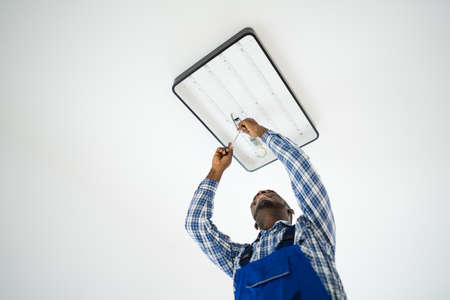 African Maintenance Electrician On Ladder Fixing And Installing Lightの写真素材