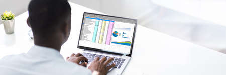 African American Man Using Spreadsheet Reports On Laptop Computerの写真素材