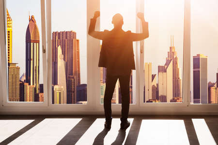 African Businessman Raising Hands. Rear View Near Window With City Downtownの写真素材