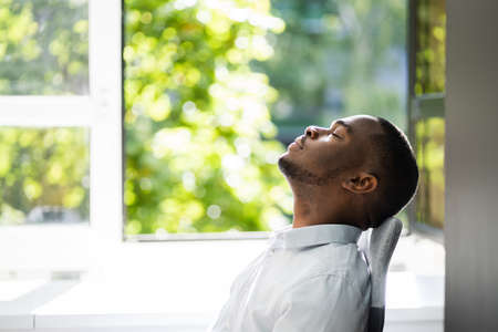 Fresh Air At Desk In Office African American Relaxing Near Windowの写真素材