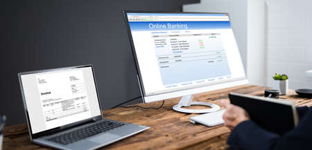 Young Businessman Looking At Invoice While Doing Online Banking On Computer