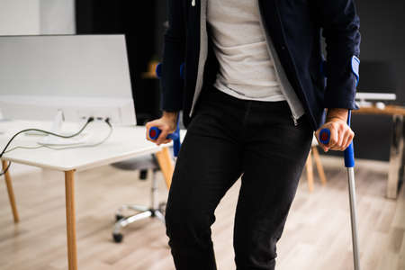 Disabled Man Standing With Crutches At Office Workplaceの写真素材