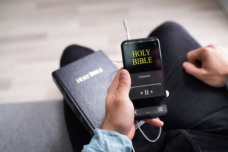 Christian Man Reading Bible Book On Phone And Prayingの写真素材