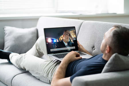 Young Man Lying On Sofa Watching Video On Tabletの写真素材