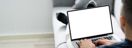 Guy Sitting On Sofa Using Laptop In Living Roomの写真素材