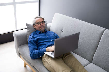 Man Using Laptop Sitting On Couch At Homeの写真素材
