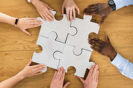 Teamwork Meeting Hands Solving Jigsaw Puzzle. Overhead View