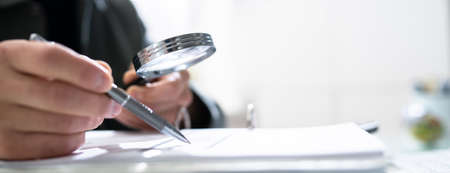 Audit And Fraud Investigation. Auditor Using Magnifying Glass On Document