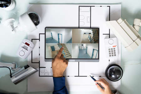 Person Watching Footage On Digital Tablet With Security Equipment On Blueprint