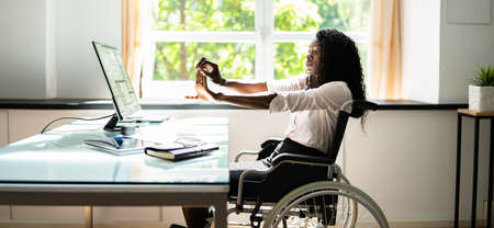 Disabled African Woman Stretching At Desk Working In Wheelchairの写真素材