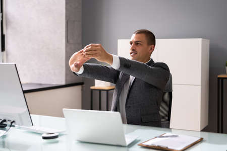 Man Doing Stretching Exercise At Desk Working On Computerの写真素材