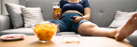 Overeating Junk Food, Drinking Beer And Watching TVの写真素材