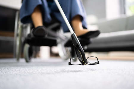 Disabled Woman In Wheelchair Using Grabber Tool Or Reacher For Fallen Glassesの写真素材