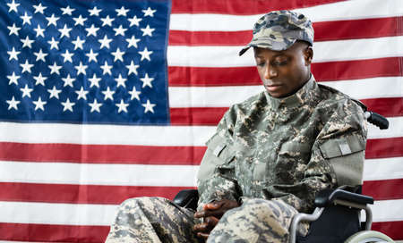 Patriotic Soldier Sitting In Wheel Chair Against American Flagの写真素材