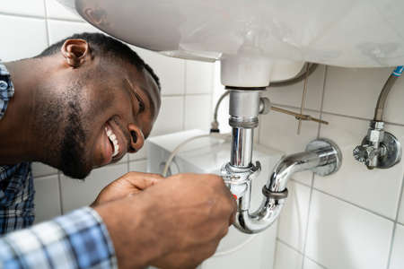 Plumber Fixing Pipe In Bathroom. Plumbing Maintenance In Bathroom