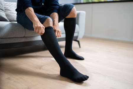 Man Putting On Medical Compression Stockings On Legsの写真素材