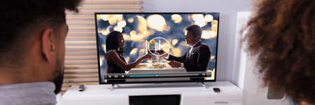 Rear View Of A Couple Watching Movie On Television At Home