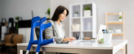 Worker With Crutches At Workplace. Social Security Compensation