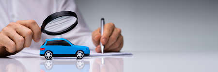 Person Scrutinizing A Car Model Using Magnifying Glass On Desk