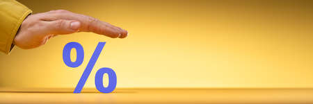 Businessperson's Hand Protecting Blue Percentage Sign Over Yellow Background