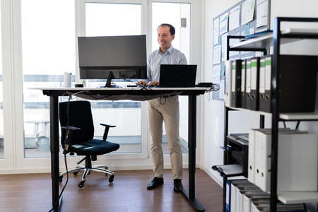 Man Using Adjustable Height Standing Desk In Office For Good Postureの写真素材