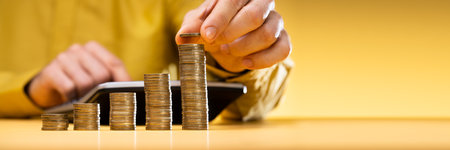 Businessman Calculating Invoice With Stacked Coins Arranged At Office Deskの写真素材