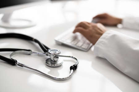 View Of Stethoscope With Doctor Using Computer Keyboard In Clinicの写真素材