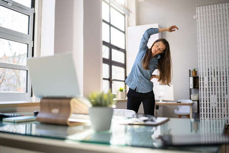 Woman In Hijab Standing And Stretching In Front Of Computerの写真素材