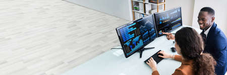 Side View Of Male And Female Stock Market Broker Analyzing Graphs On Laptop At Workplaceの写真素材